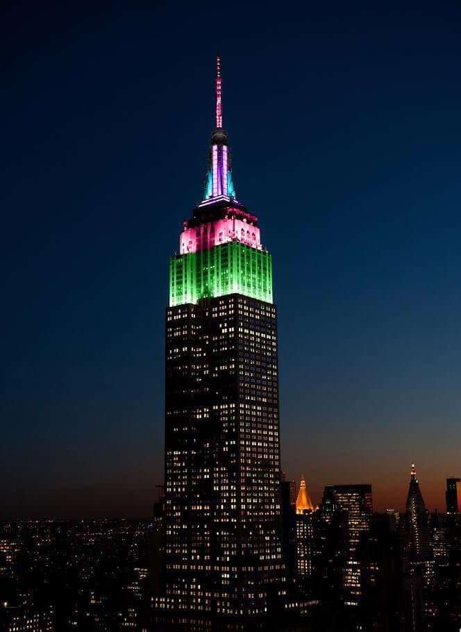 Image of The Empire State Building in New York, lit up at night in blue, pink and green, in honor of Rare Disease Day