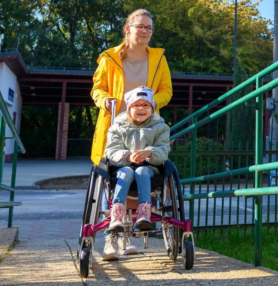 Mother walking her son in a wheelchair outside, smiling
